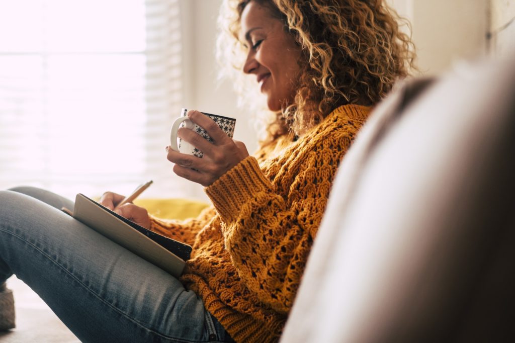 Happy cute lady at home write notes on a diary while drink a cup of tea and relax