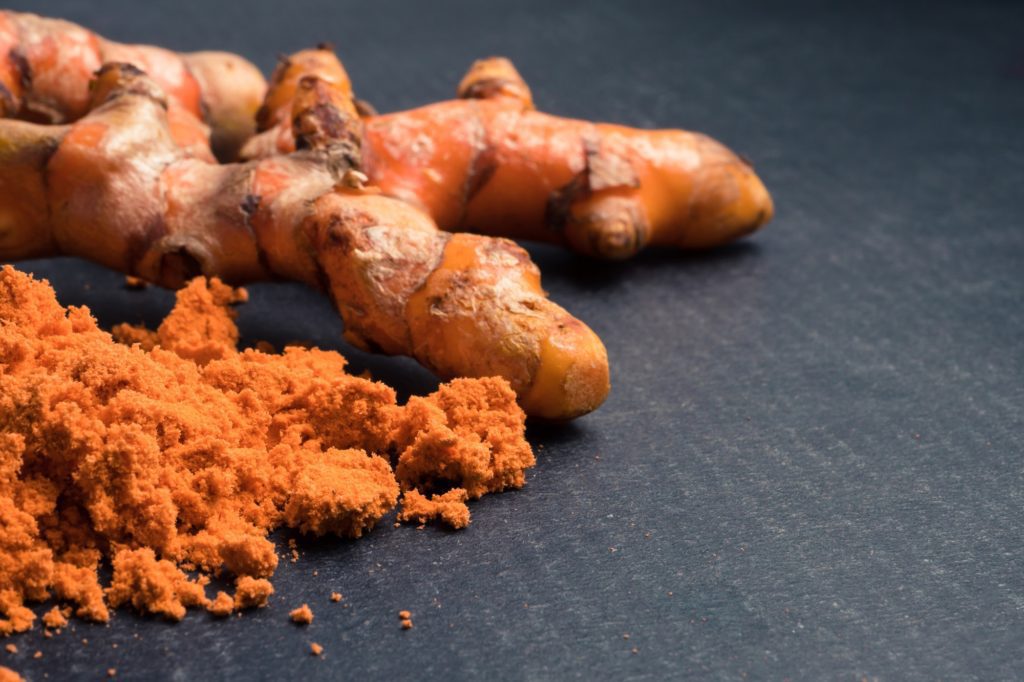 Turmeric roots with turmeric powder on black background.