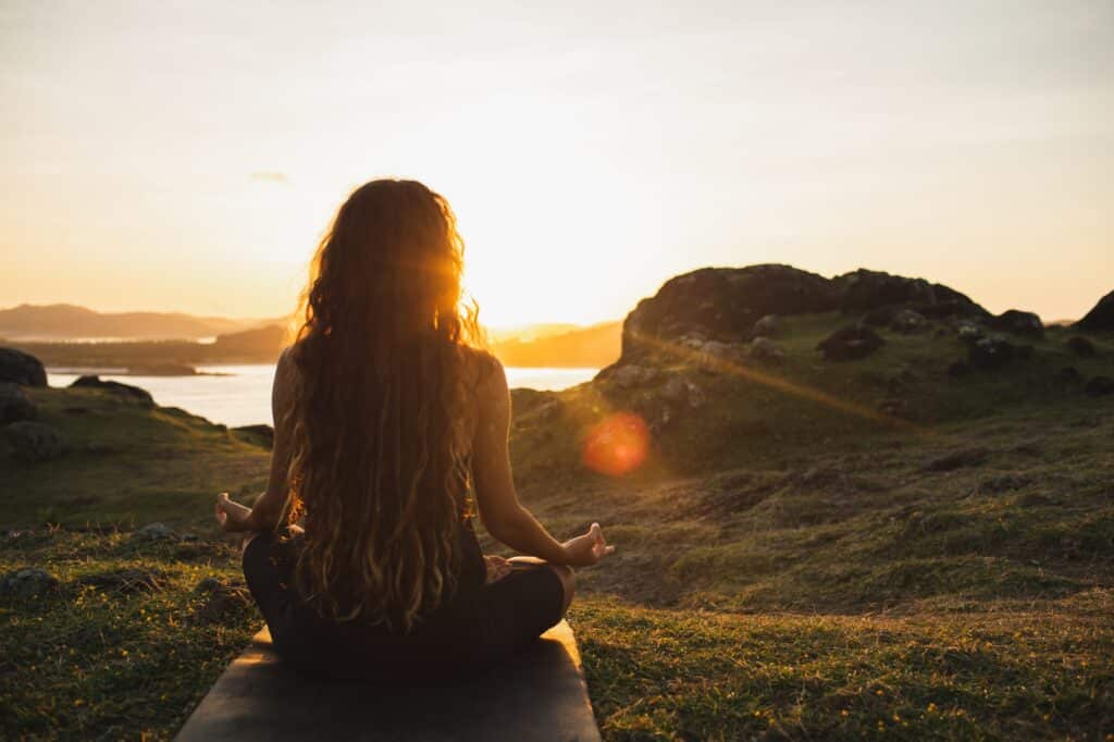 Woman meditating yoga alone at sunrise mountains. View from behind. Travel Lifestyle spiritual