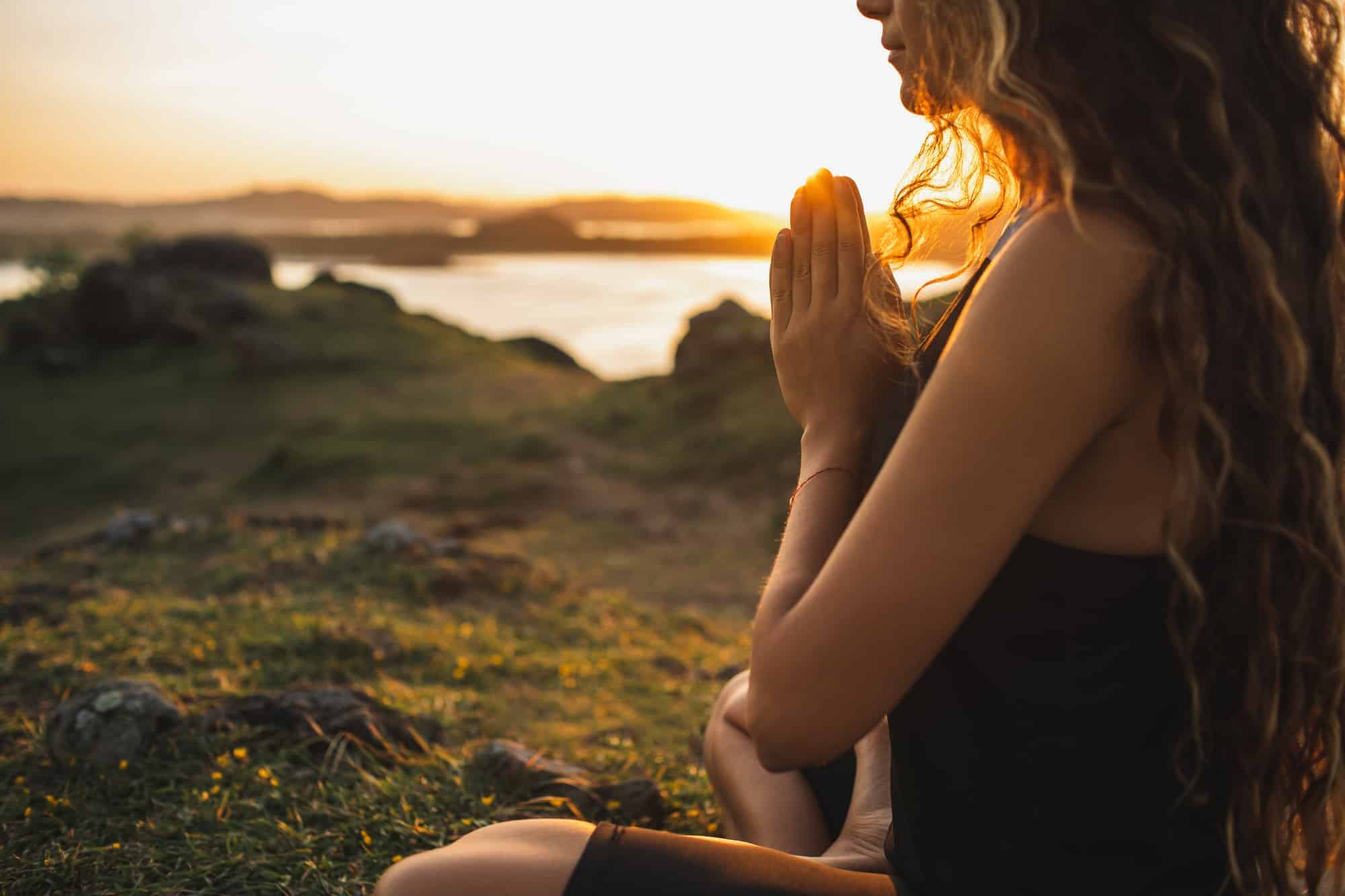 Woman praying alone at sunrise. Nature background. Spiritual and emotional concept