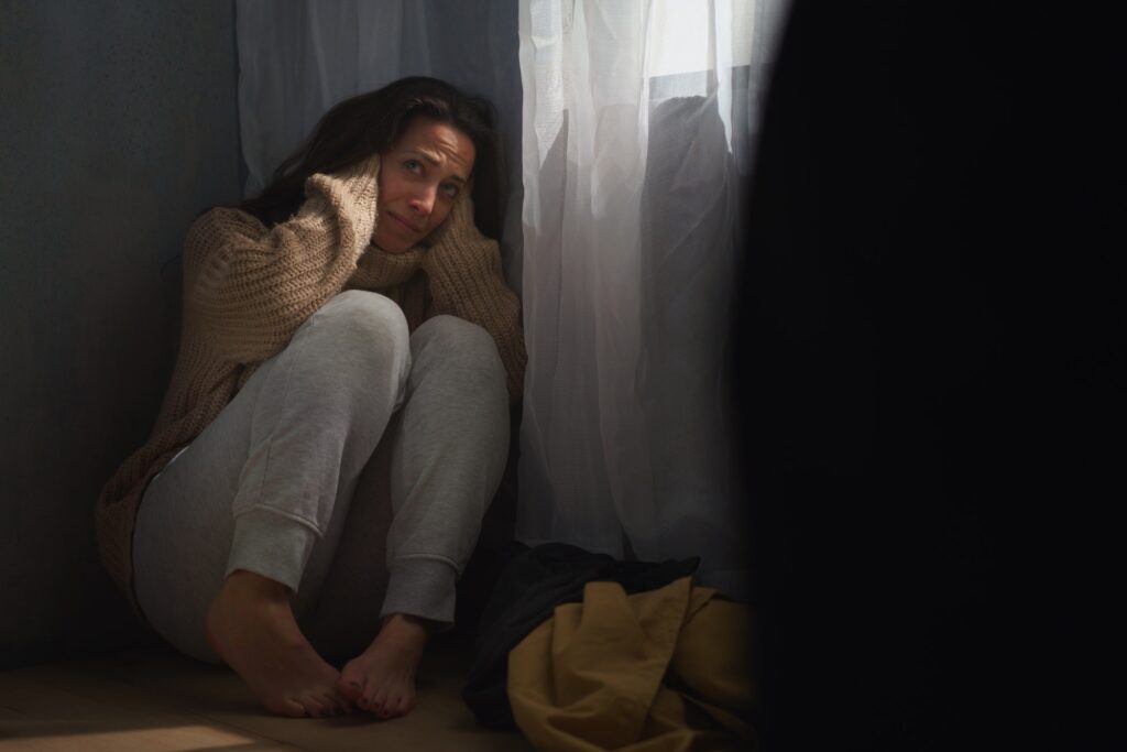 Scared woman sitting on ground and covering her head in fear of domestic violence