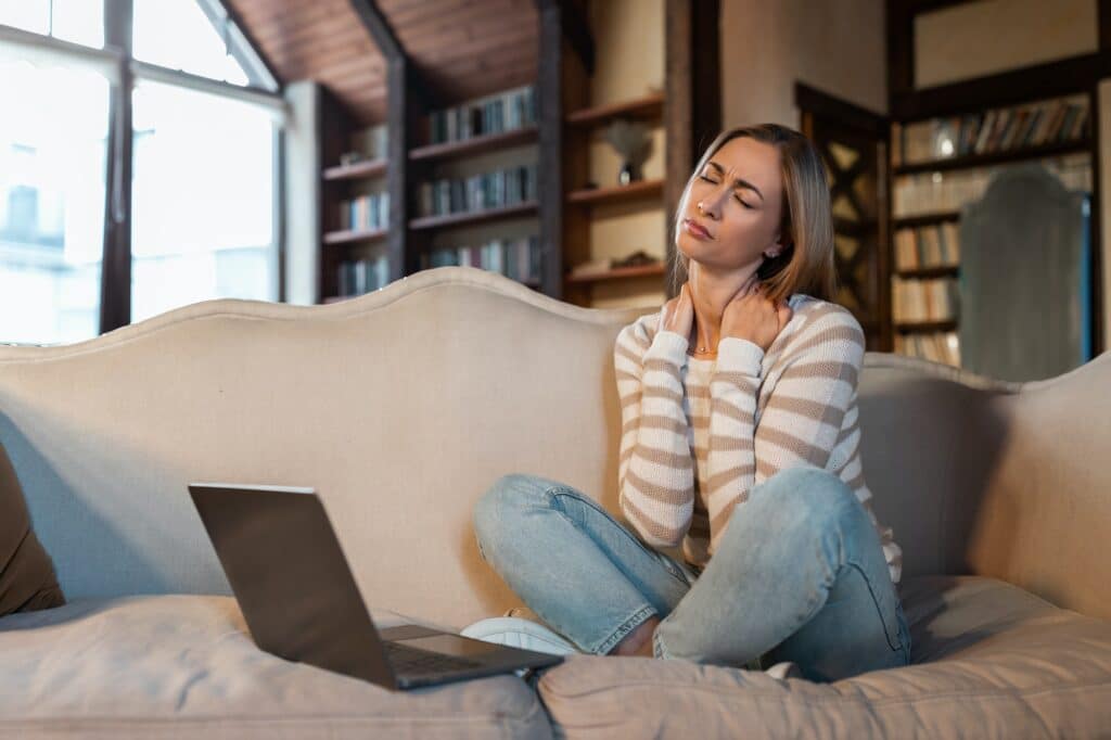 Tired woman sitting on couch with pc, massaging neck